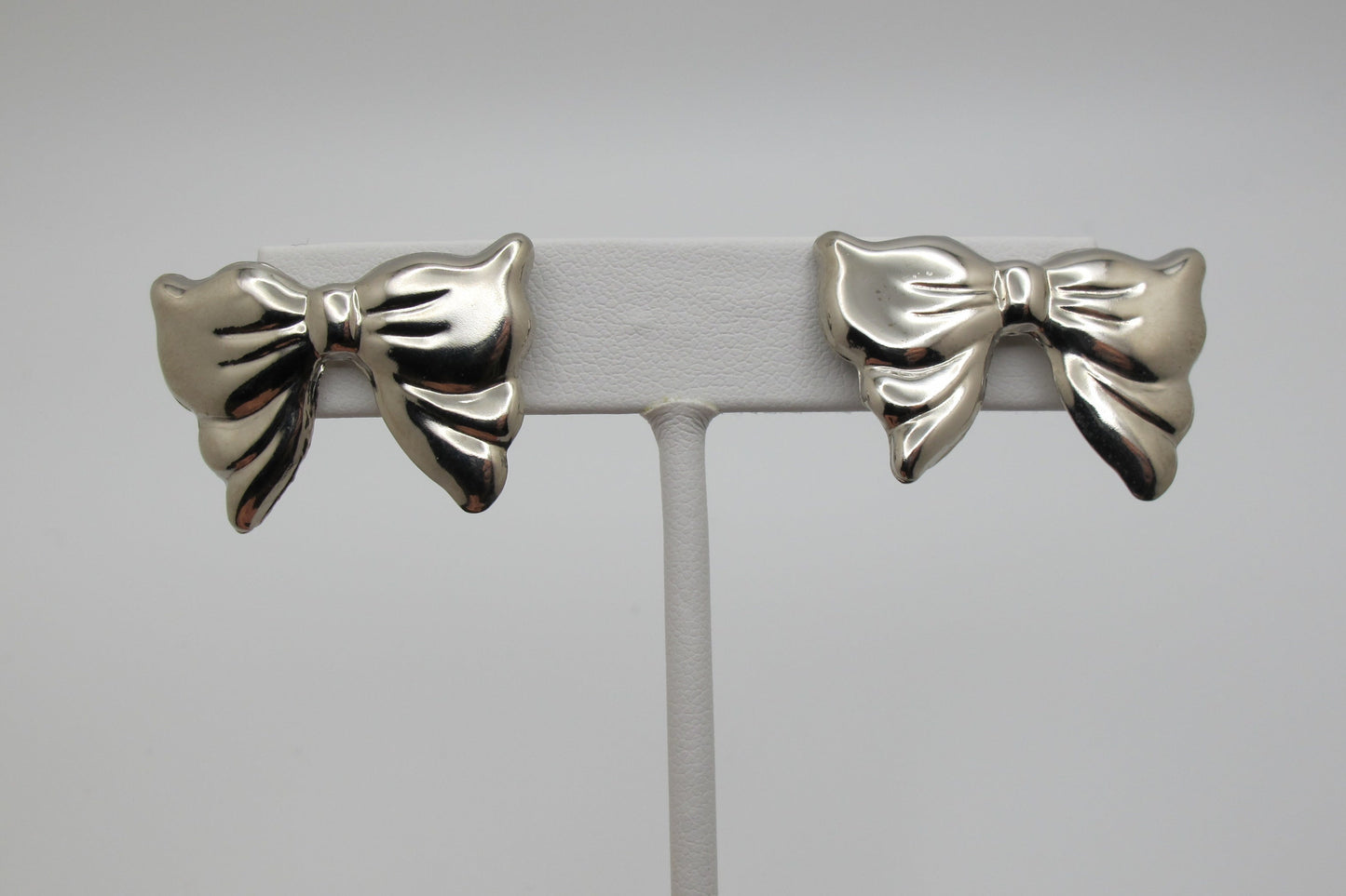Silver bow-shaped earrings on a gray stand against a light gray background