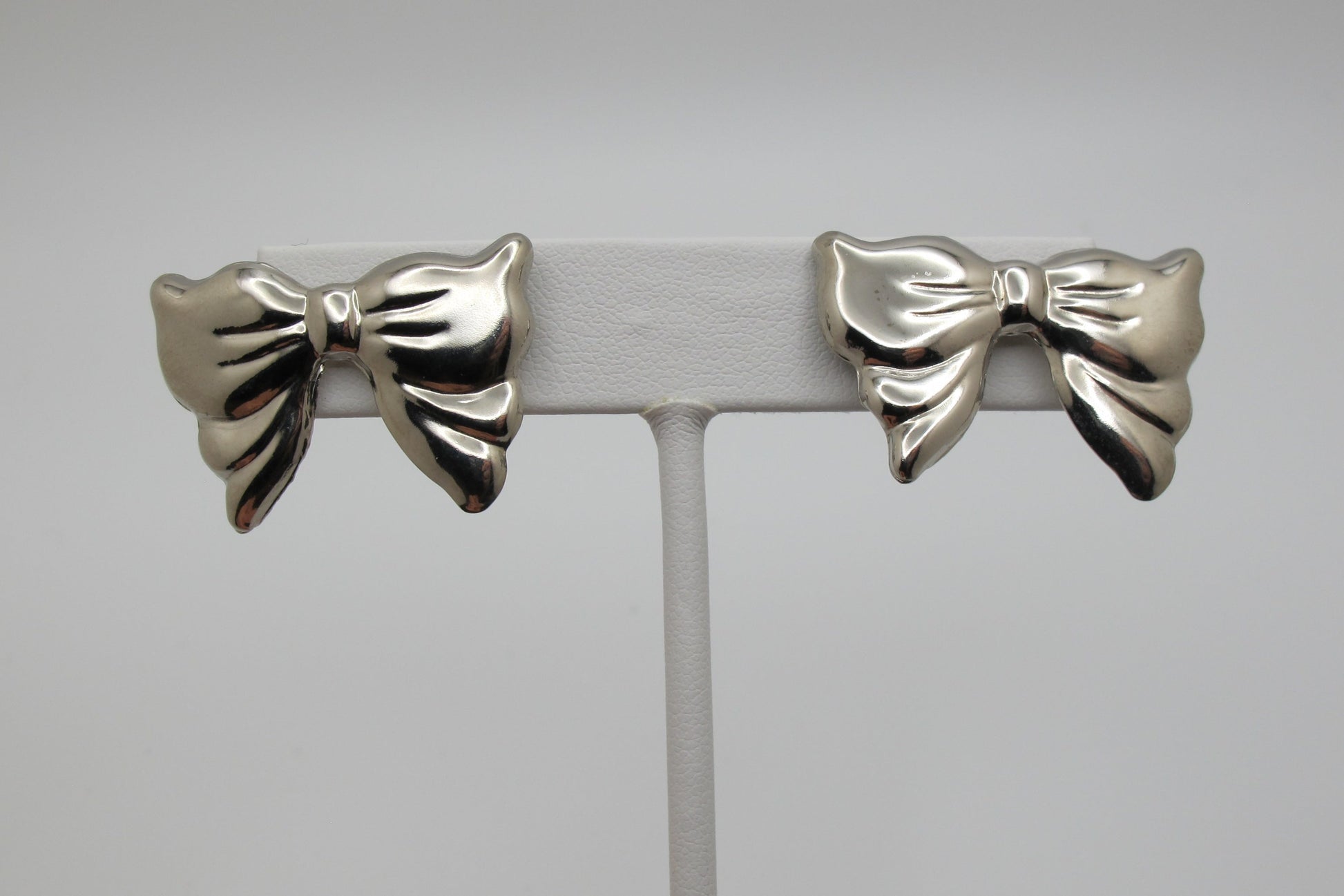 Silver bow-shaped earrings on a gray stand against a light gray background