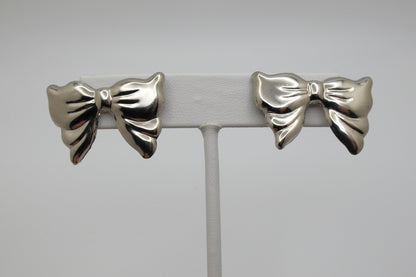 Silver bow-shaped earrings on a gray stand against a light gray background