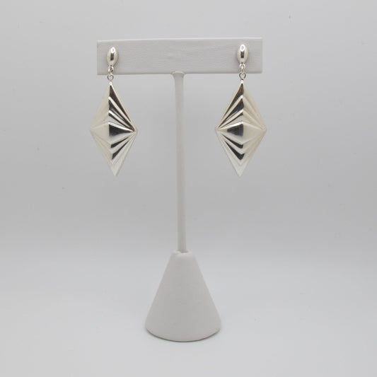 Pair of silver geometric earrings on a white stand against a white background